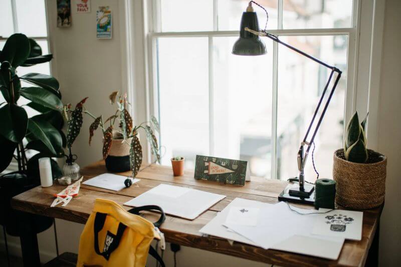 bright, airy room with plants, task lamp, and wooden desk with papers - Lumilum