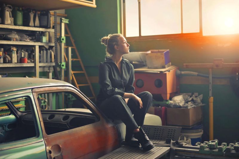Woman sitting on hood of car in garage - Lumilum