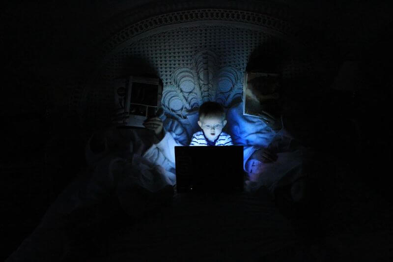 boy in front of bright blue light emitted from laptop in a dark room - Lumilum