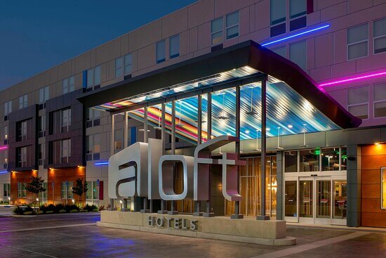 aloft hotel exterior front with "aloft hotels" sign illuminated with pink and blue led strip lights