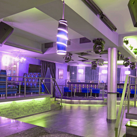 purple and green hued banquet hall with blue accent furniture, lighting projectors on ceiling, and a disco ball