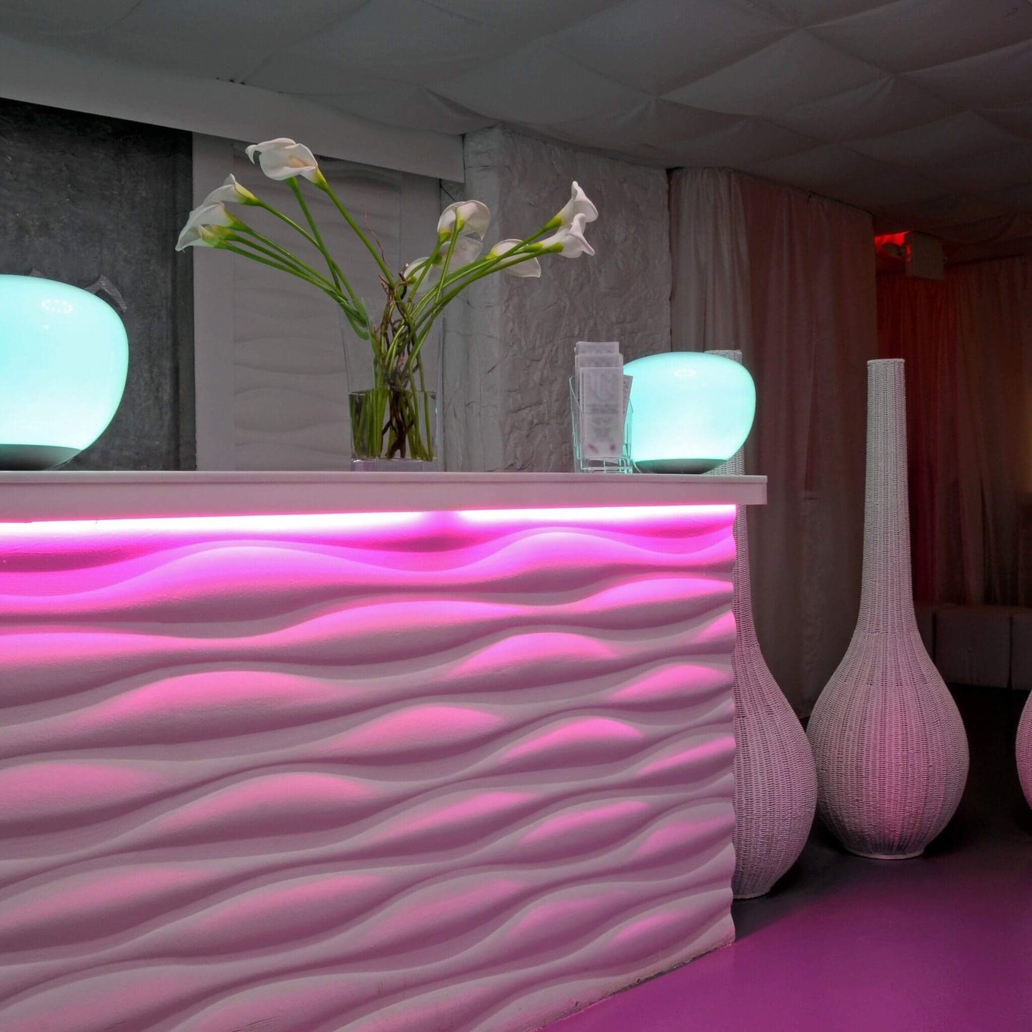 pink hued hotel lobby with waveform counter and flower vase. A pink led strip light is seen giving intense pink light from under counter
