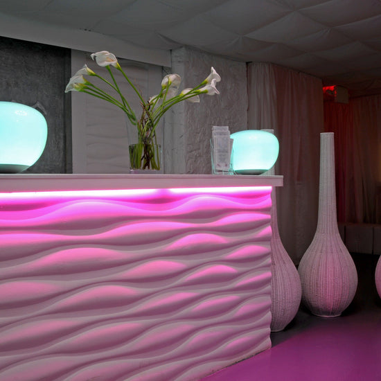 pink hued hotel lobby with waveform counter and flower vase. A pink led strip light is seen giving intense pink light from under counter