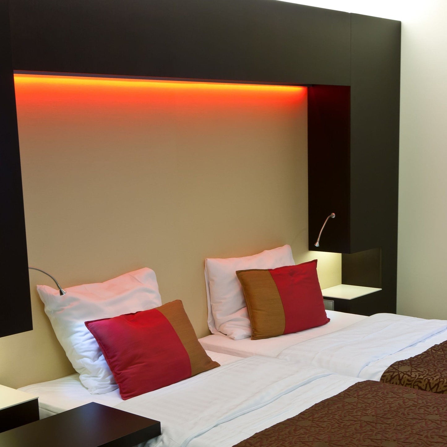 hotel room double beds illuminated by orange strip light installed in modular black wall casing